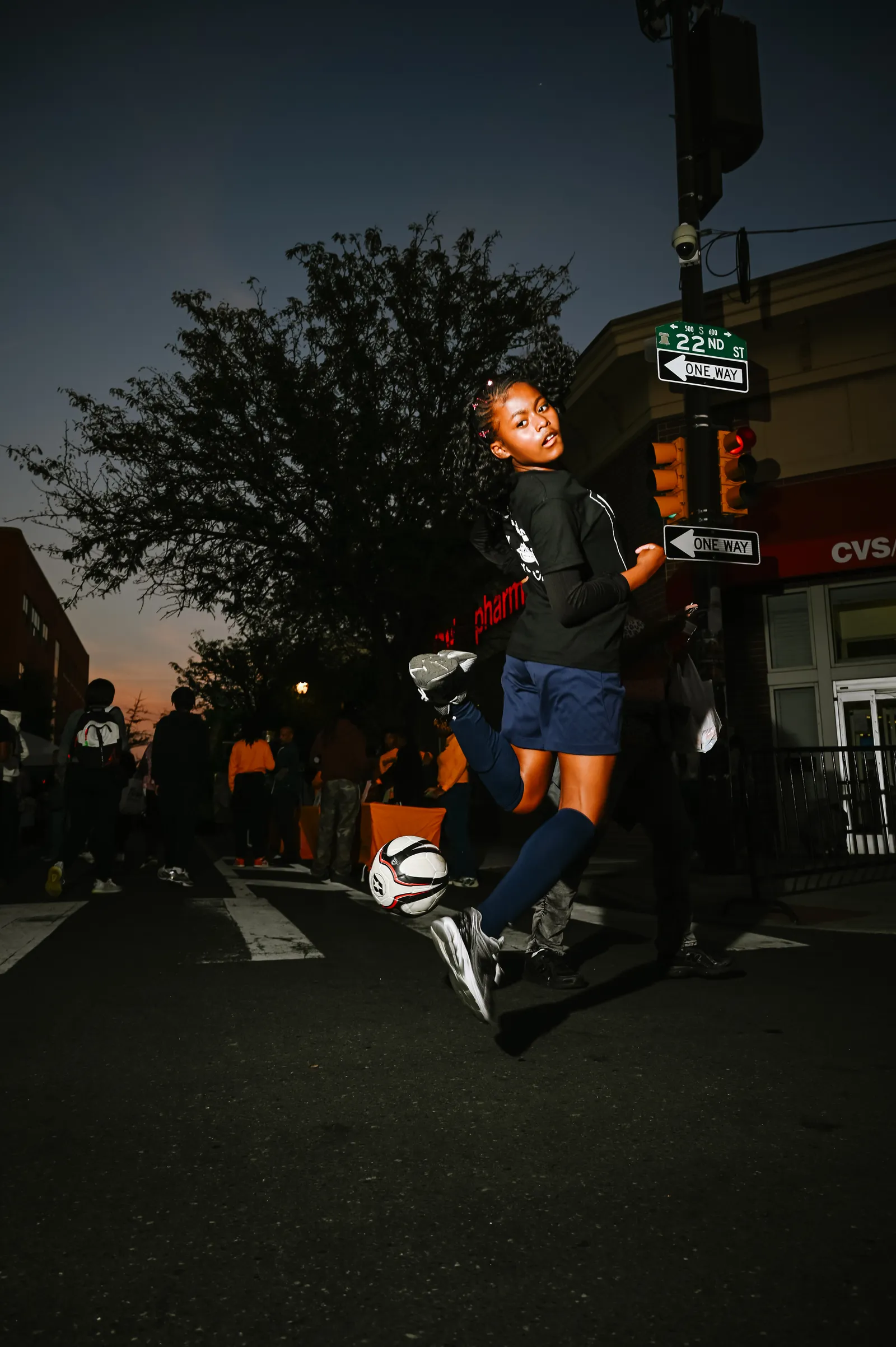 Young athlete jumping with soccer ball on city street at dusk