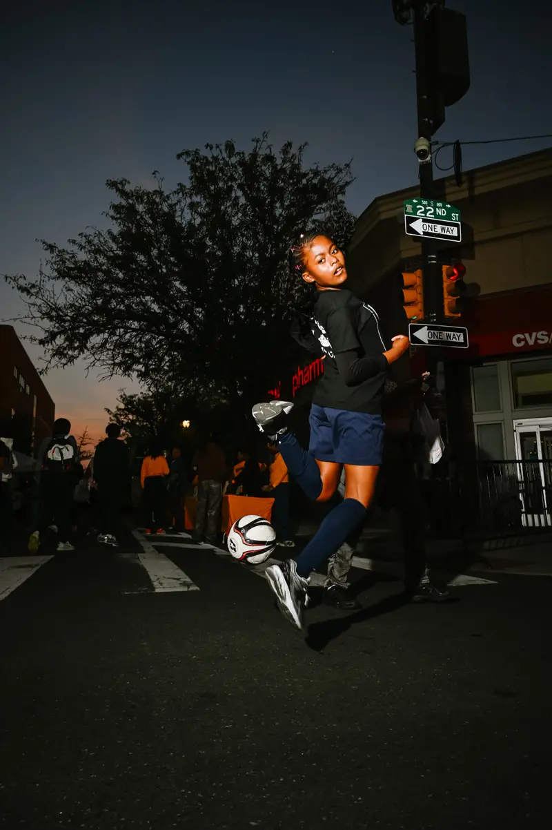 Young athlete jumping with soccer ball on city street at dusk